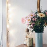 A cozy interior featuring a floral arrangement in a vase, with string lights and a mirror creating a warm atmosphere.
